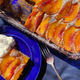 Tranche de gâteau aux pêches de Baltimore sur plaque bleue avec une fourchette à côté du plateau plein de gâteau